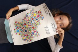 Poster sulla mostra di Mauro Bubbico tenuto tra le mani da una bambina sdraiata a terra